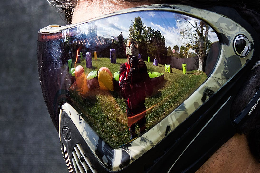 A man wearing a mask shows the reflection of another man taking aim.